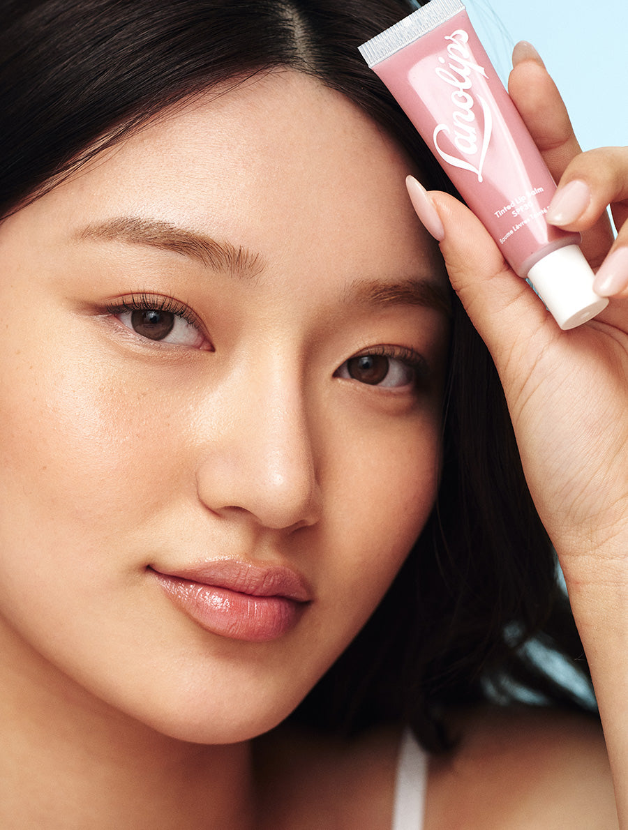 Model holding tube of Lanolips Tinted Lip Balm SPF30 in Perfect Nude