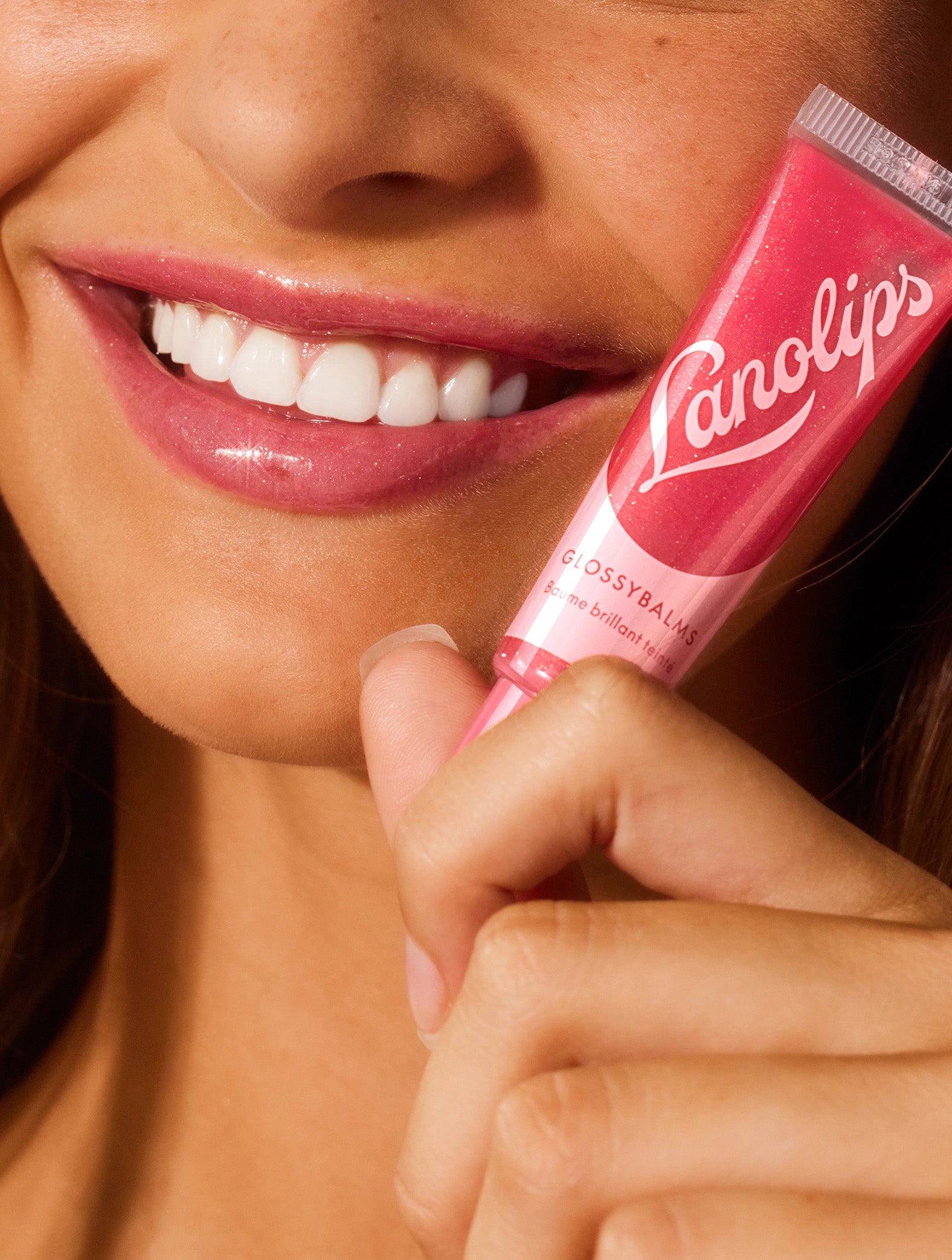Close up image of a model holding a tube of lanolips glossy balms candy lip balm.