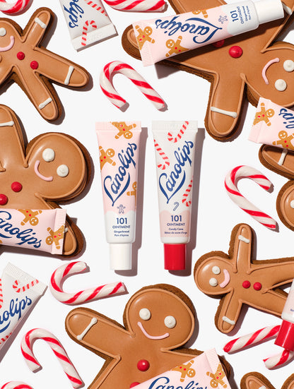 Lanolips 101 Ointment Multi-Balm Gingerbread & Candy Cane centred among gingerbread cookies, candy canes and balm tubes, from the Lanolips Holiday Gingerbread House Lip Duo. Hydrating lanolin, vitamin E and natural flavours keep lips soft and festive.