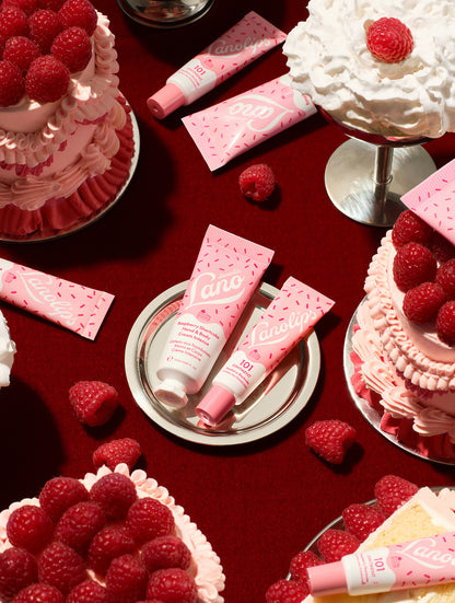 Lanolips Raspberry Shortcake Holiday Duo – 101 Ointment Multi-Balm and Hand & Body Cream Intense, styled with raspberry shortcake, whipped cream and fresh raspberries on a red background.