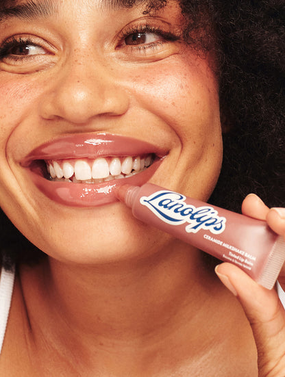Close-up of smiling model holding Lanolips Ceramide Milkshake Balm in Caramel Melt, with smooth, glossy lips and a rosy-caramel nude tint
